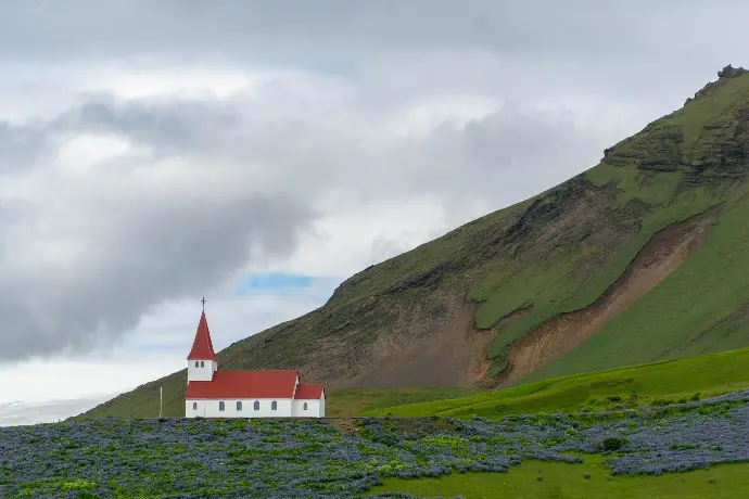 white and red concrete building near green mountain under white clouds during daytime